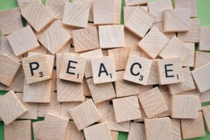 Pile of blank scrabble tiles on a green background, with the letters spelling PEACE in the middle