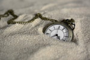 Pocket watch with Roman numerals and a chain, half buried in sand