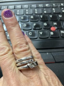 Fingers with rings, one of which says "I am enough"