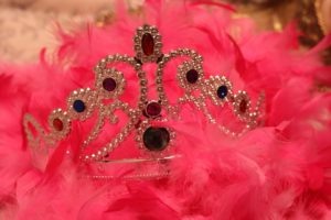 Gold tiara with colourful stones, set on a background of a pink feather boa.