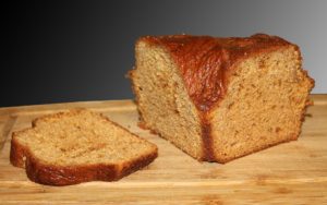 wooden board with black background, loaf of honey cake with one slice cut off and laid to one side