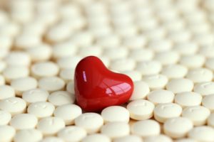 Red shiny heart-shaped gem resting in a field of white medicine tablets