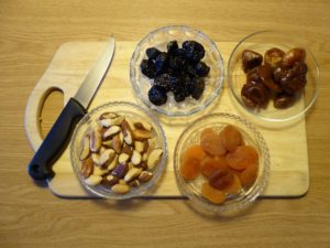 Brown table and cutting board with a knife and glass bowls of dried fruit and nuts.