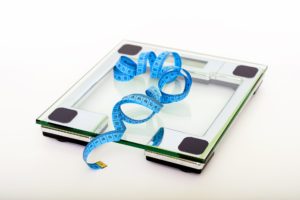 Glass body weight scale with a blue measuring tape on top of it