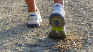 White feet running in white, blue and yellow runners on a pebbly path