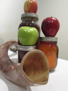 Red and green apples and a jar of honey artistically piled together, with a shofar in the foreground