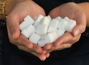 Two cupped white hands filled with white sugar cubes on a black background.