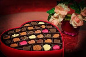 Pink-suffused picture of a heart-shaped box full of assorted chocolates, and a vase with pink and white roses