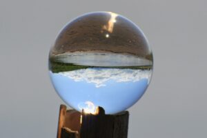 Crystal ball with upside down landscape inside, brown and water on the top, blue sky and white clouds at the bottom.