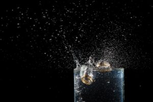 Two wedding rings splashing into a glass of beverage on a black background with bubbles