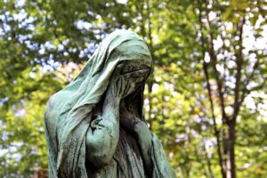 Weeping bronze statue, with blurred green trees in the background