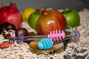 A scene with pomegranates, apples and honey servers on a bed of wood shavings