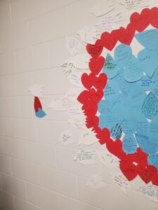 A white wall with white dove shaped, red heart shaped and blue teardrop shaped papers attached to it, with writings of grief and hope on them